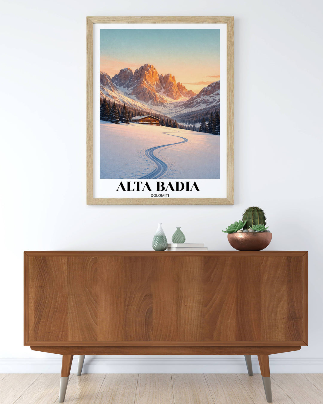A wooden vertical framed wall art poster of Alta Badia in the Dolomites, featuring a deep S-curve ski track leading to a glowing mountain chalet under a golden sunset.