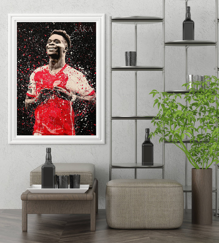 Bukayo Saka poster showing the Arsenal FC forward celebrating with arms crossed over his badge, illustrated in a bold splatter-art aesthetic that suits any North London football fan&
