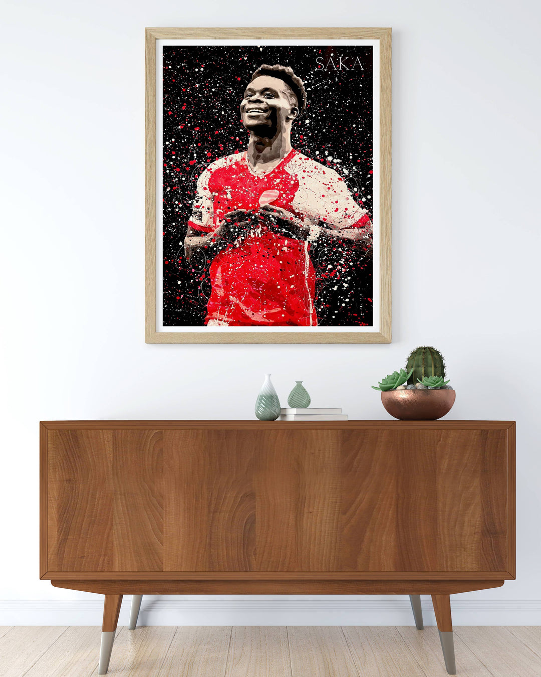 Arsenal FC player poster featuring Bukayo Saka in a splatter-art illustration style, set against a black background with red and white paint texture, celebrating the North London club&