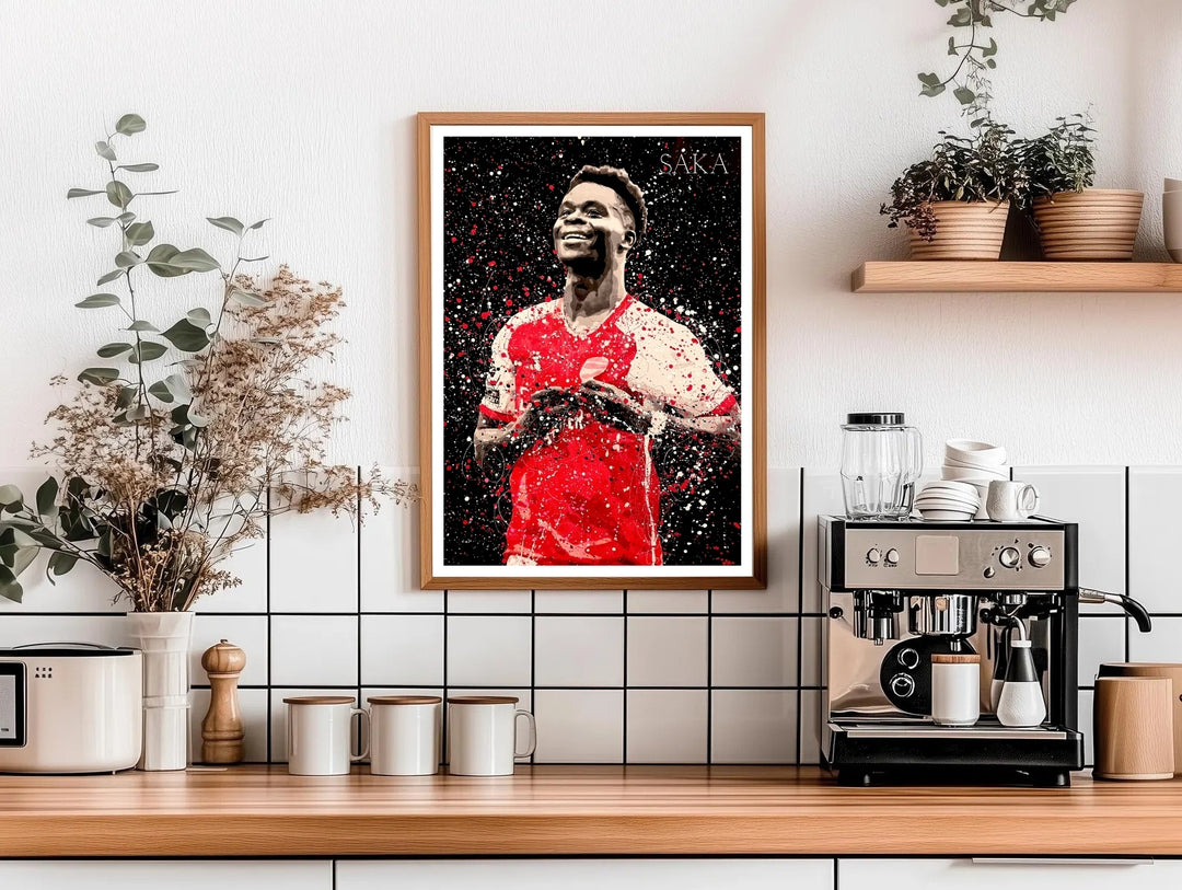 Football poster of Bukayo Saka in Arsenal FC kit, illustrated with a dramatic paint-splash effect against a dark background, a striking piece of North London sports wall art available as canvas, framed, or unframed wall art.