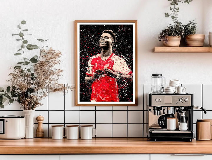 Football poster of Bukayo Saka in Arsenal FC kit, illustrated with a dramatic paint-splash effect against a dark background, a striking piece of North London sports wall art available as canvas, framed, or unframed wall art.