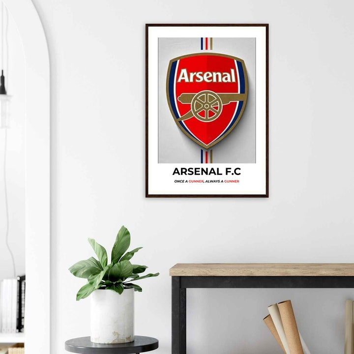 Framed Arsenal F.C. poster on a wall above a desk with a plant.