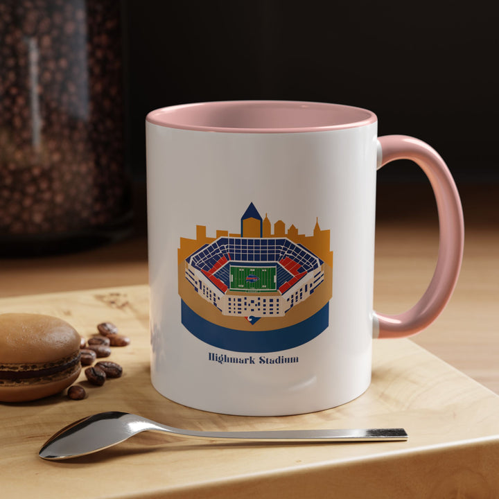 Pink Highmark Stadium Mug featuring a detailed stadium illustration wrapped around the exterior, shown in a cozy setting with soft lighting to highlight the warm and cheerful tone of the pink ceramic. Perfect for Buffalo Bills fans who enjoy adding a touch of personality and color to their coffee, tea, or hot chocolate moments while proudly celebrating their home stadium every day.