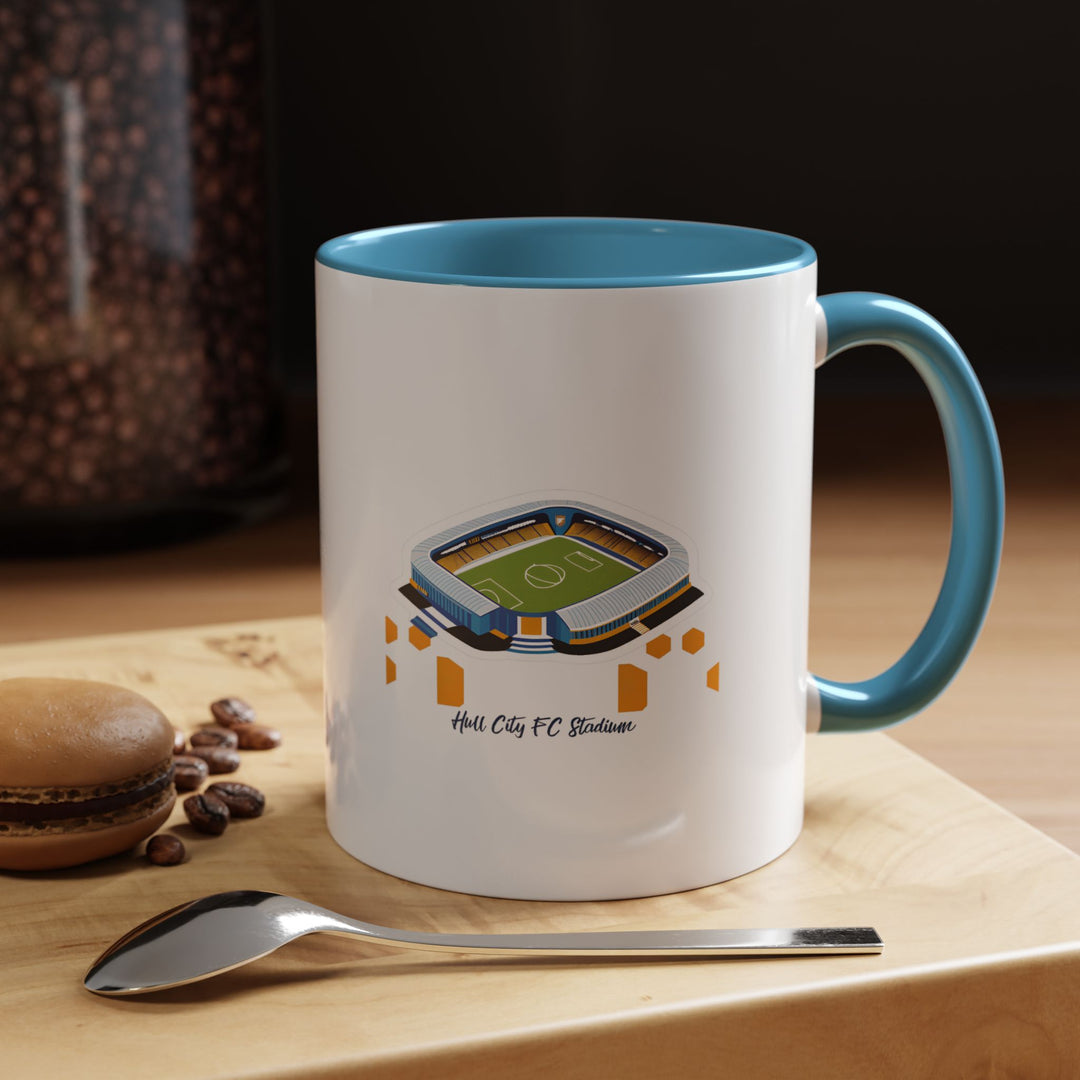 A blue Hull City FC stadium mug displaying a panoramic illustration of MKM Stadium printed with high clarity. The calming blue tone pairs well with the artwork, seen here in a relaxed workspace setting, capturing the comfort of enjoying tea or coffee while staying connected to the passion of supporting Hull City throughout the day.