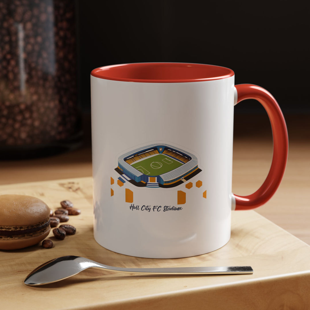 A Hull City FC MKM Stadium mug with a bold red ceramic exterior, featuring detailed stadium artwork wrapped around the surface. Shown on a kitchen table with natural daylight emphasizing the vivid color and crisp illustration, perfect for fans who enjoy starting their morning coffee with pride for The Tigers and their home ground.