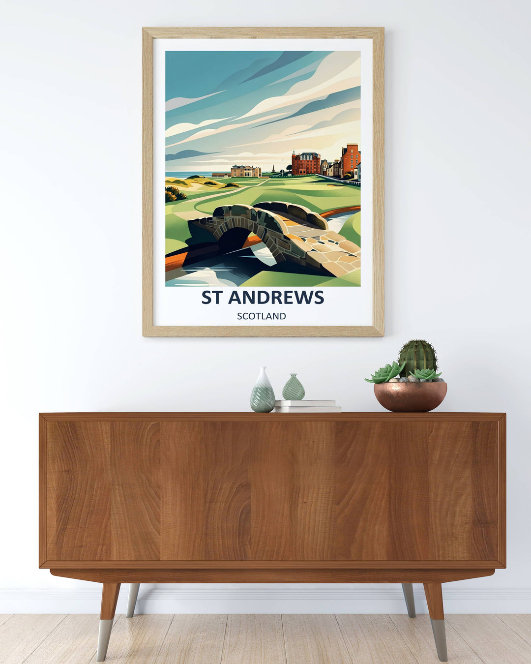 A modern graphic illustration of the 18th hole at St Andrews Old Course in Scotland, showcasing the historic stone Swilcan Bridge crossing a calm stream with the Royal and Ancient Clubhouse and red-brick hotel under a stylized, layered blue and cream sky.
