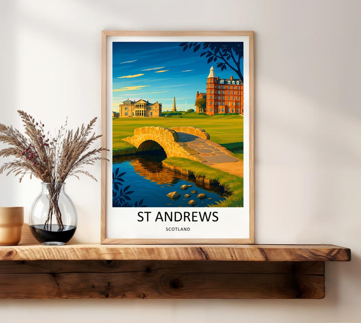 Framed travel poster of the legendary Old Course in St Andrews Scotland, displaying a unique perspective of the 18th green, the famous footbridge over the burn, and grand red-brick luxury resort buildings in the background.