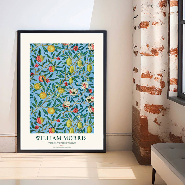 Ripe lemons, blushing peaches, and cut pomegranates hanging from leafy olive branches over a vibrant sky blue background in an 1862 William Morris Fruit art print.
