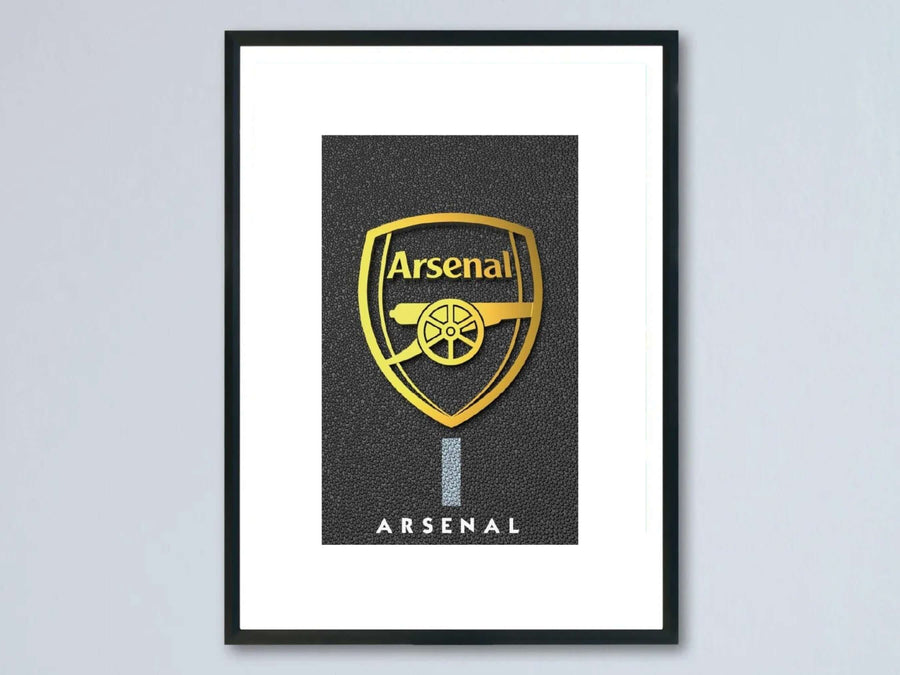 Framed metallic gold Arsenal FC crest poster featuring a shiny golden club shield and cannon logo over a premium textured pebble black background, showcased inside a modern black photo frame.