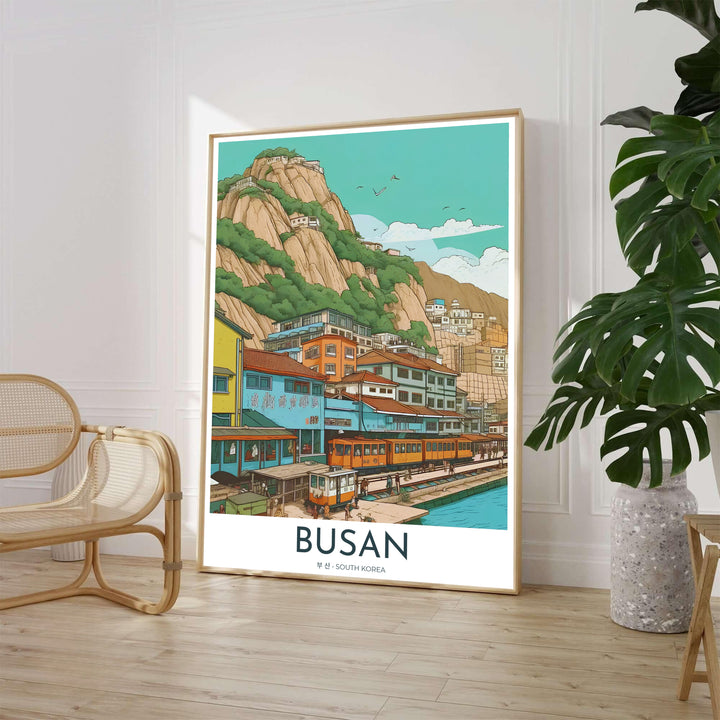 Retro comic style travel poster of Busan, South Korea, featuring a coastal yellow train running alongside a picturesque seaside village nestled against dramatic rocky cliffs. Offered by MapYourDreams, this artwork is available in flexible options including unframed paper, custom wooden frames, and gallery canvas wraps.