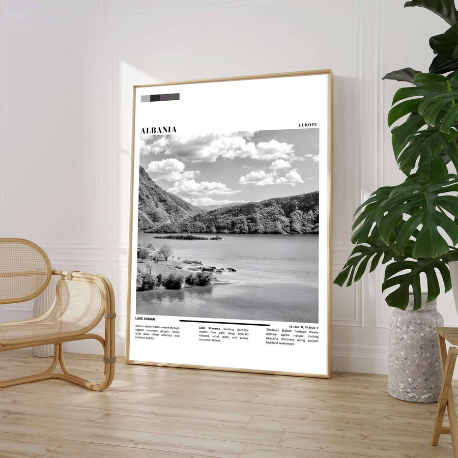 A sleek black and white landscape print showcases the fjord-like waters and rugged mountain slopes of Lake Koman under a cloudy sky. Customers can select from unframed archival paper stock, custom wood frames, or gallery canvas wraps to suit their home interior style preferences.