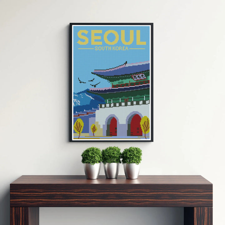 Picturesque cross-stitch landscape artwork showing Gwanghwamun Gate in Seoul, South Korea, rendered with intricate micro-patterned stitches against a crisp blue sky and yellow header text. Offered by MapYourDreams, this artwork is available in flexible options including unframed paper, custom wooden frames, and gallery canvas wraps.