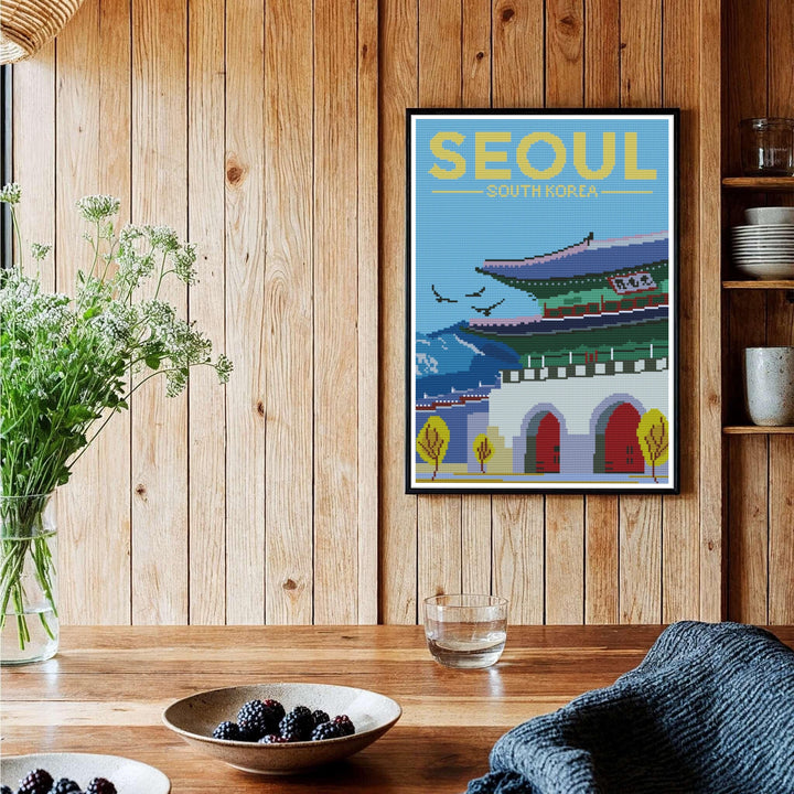 Folk-art inspired cross-stitch wall decor capturing the grand entrance of Gwanghwamun Gate in Seoul, South Korea, with vibrant jade green, crimson red, and bright sky-blue needlework patterns. Offered by MapYourDreams, this artwork is available in flexible options including unframed paper, custom wooden frames, and gallery canvas wraps.