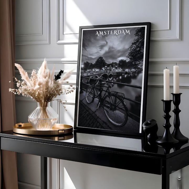 Black and white photo poster depicting lit bridge arches, glowing townhouses, and a parked bike along an Amsterdam canal, crafted by MapYourDreams with choices available for an unframed paper print, a ready-to-hang gallery canvas, or custom framed wall art designed for modern industrial spaces.