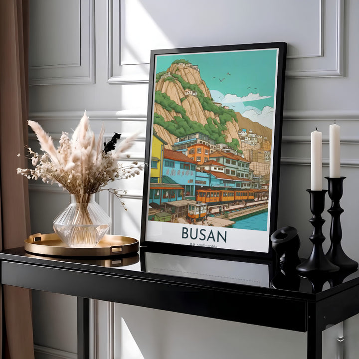 Serene Asian landscape print capturing a coastal railway line in Busan, South Korea, with pastel blue, yellow, and orange buildings cascading down a green hillside to the sea. Offered by MapYourDreams, this artwork is available in flexible options including unframed paper, custom wooden frames, and gallery canvas wraps.
