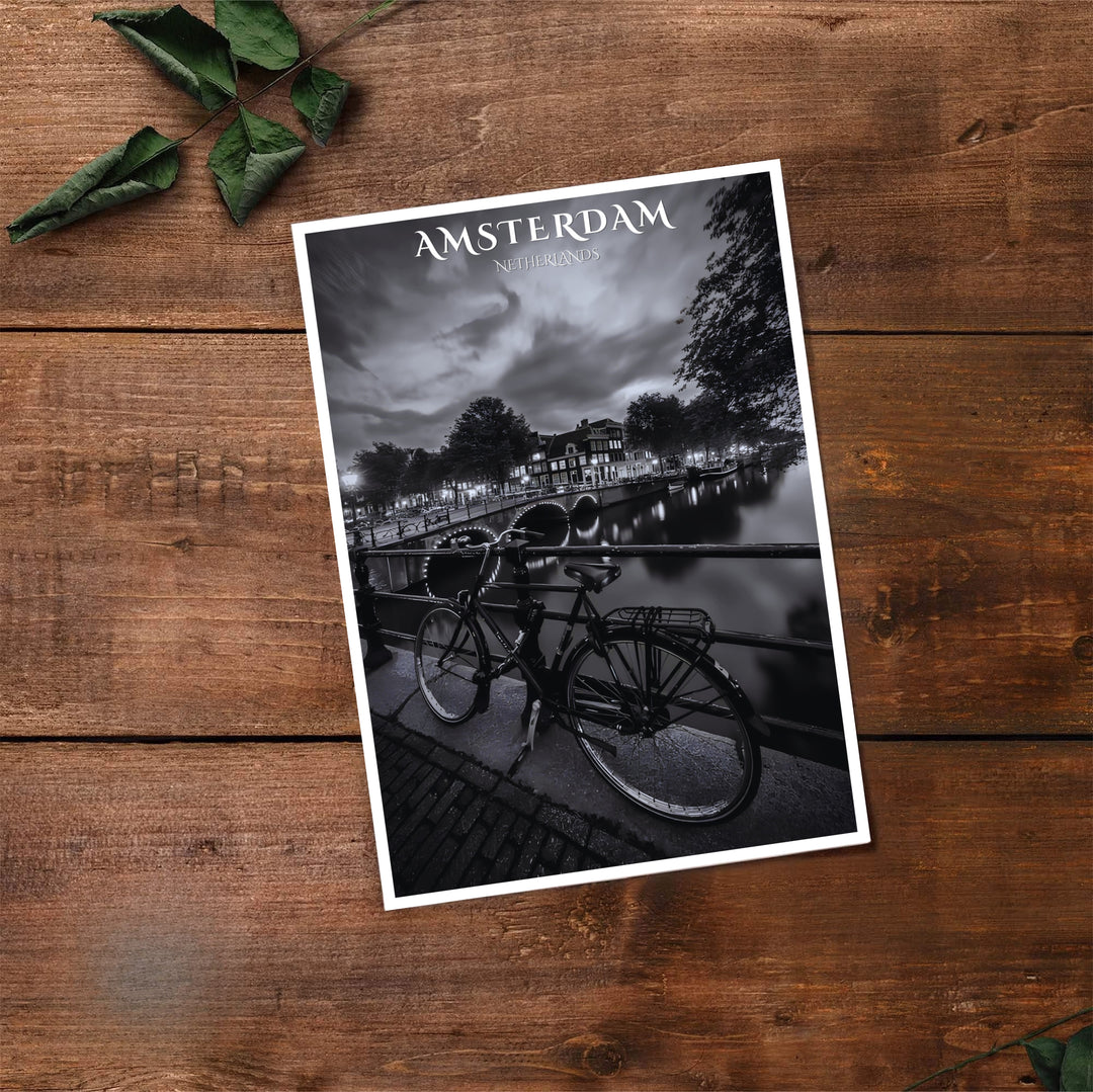 Cinematic black and white travel print of historic Amsterdam canal houses paired with a parked bike and bridge reflections, available at MapYourDreams where you can select from unframed paper prints, gallery canvas, or custom framed wall art options for modern interior spaces.