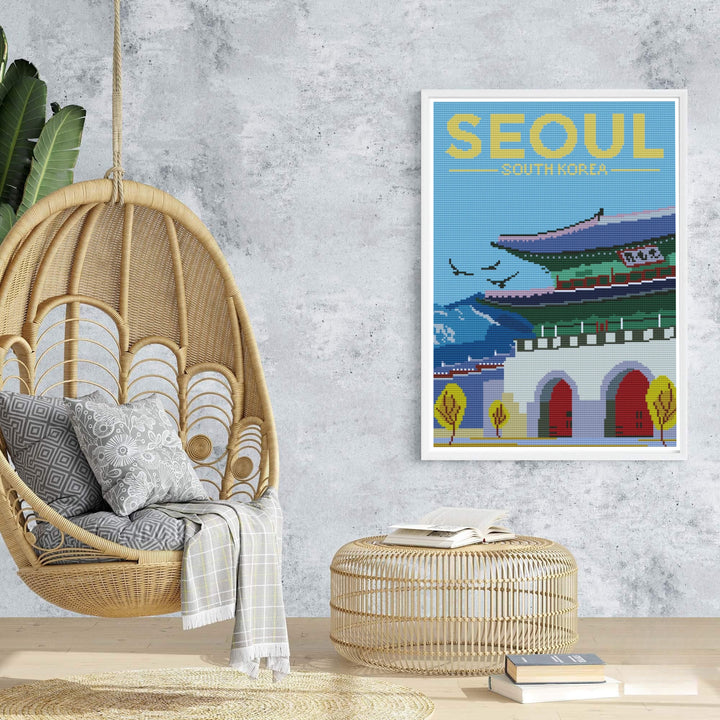 Sophisticated needlework travel poster of Seoul, South Korea, presenting a detailed cross-stitch depiction of Gwanghwamun Gate with prominent yellow headline text and mountain silhouettes. Offered by MapYourDreams, this artwork is available in flexible options including unframed paper, custom wooden frames, and gallery canvas wraps.